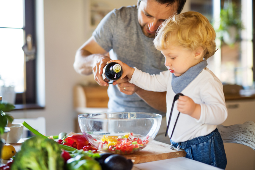father showing toddler how to make a salad